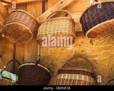 Beautiful woven willow baskets hanging on wooden wall of rustic store Stock Photo