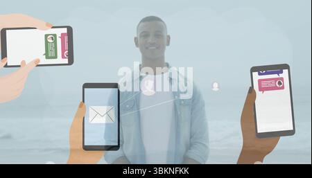 Standing man wearing denim shirt and white tee on sandy shore, with floating messaging smartphones Stock Photo