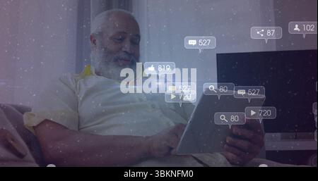 Senior Middle Eastern man wearing pale shirt holding tablet, viewing floating icons in living room Stock Photo