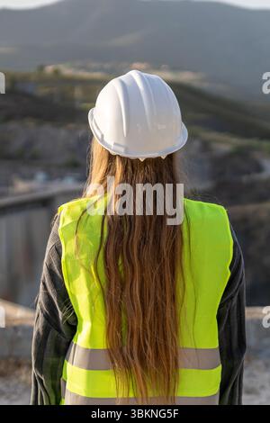 Female engineer overseeing construction site wearing safety vest and helmet Stock Photo