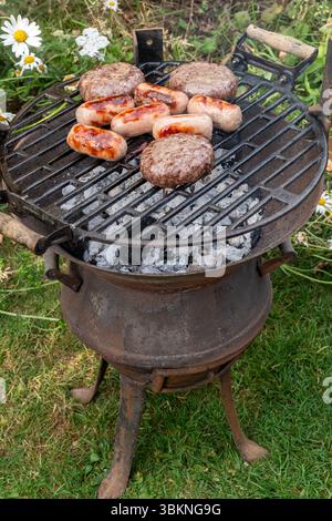 Sausages and beefburgers cooking on a barbecue on a garden pot belly stove, England, UK Stock Photo