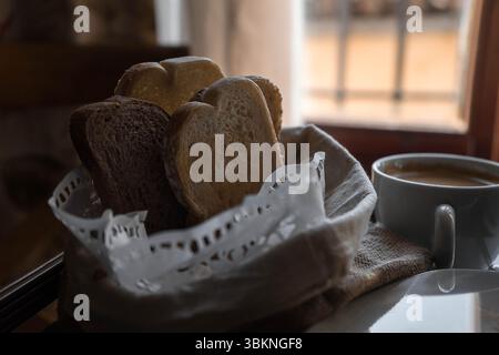 A still life image featuring a white basket filled with assorted breads placed next to a cup of coffee on a table Stock Photo