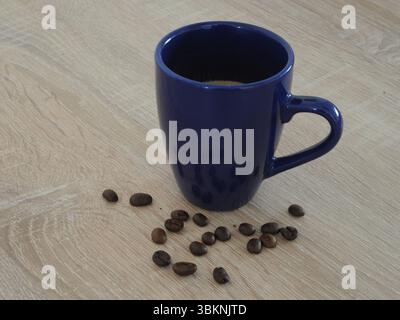 Small blue cup of coffee or espresso with some coffee beans on a wooden table. A means to wake up in the morning. Stock Photo