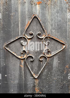 Decorative wrought iron detail on textured dark metal surface with rust and peeling paint. Ideal for design, background, or texture use. No people. Stock Photo
