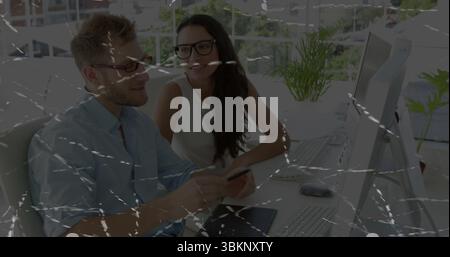 Discussing project two colleagues reviewing smartphone details at office desk, with monitor, plant Stock Photo