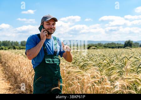 Male agricultural worker giving thumbs up during phone call at cereal field Stock Photo