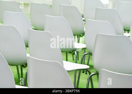 A row of white chairs is arranged in a large conference room. The chairs are empty, and the room is empty. Stock Photo