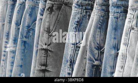 Row of jeans with different shades of blue. The jeans are hanging on a rack. The jeans are of different shades of blue, with some being darker and som Stock Photo