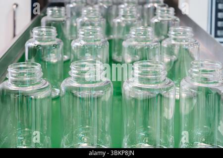 Empty plastic transparent bottles for pharmaceuticals, cosmetics and household chemicals stand in rows on an industrial conveyor belt at a factory Stock Photo
