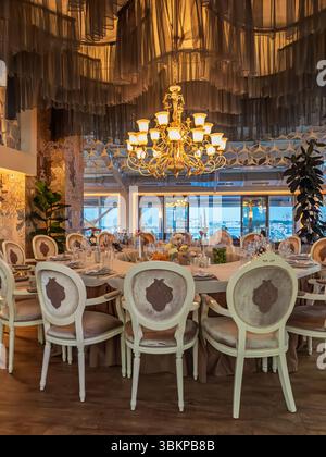 Elegant banquet hall with a beautifully set round table for a wedding or gala dinner. Luxurious interior with a classic golden chandelier and vintage Stock Photo