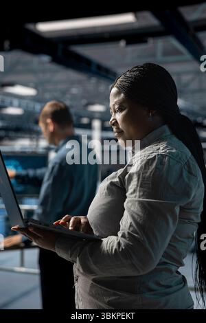 Server farm colleagues working together, running diagnostics on infrastructure using laptop. Teamworking data center engineers deploying new builds to improve uptime using notebook Stock Photo