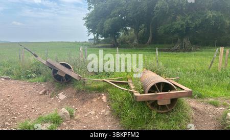 Rusty abandoned farm rollers resting in overgrown grass, showing weathered metal and rural decay in the Scottish countryside. Stock Photo