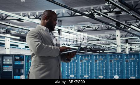 Smiling data center technician installing and upgrading hardware components. Happy server farm employee doing job tasks, implementing backup solutions to protect against data loss, camera A Stock Photo