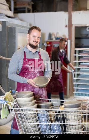 Enthusiastic ceramicist demonstrating handcrafted plates in ceramic studio Stock Photo