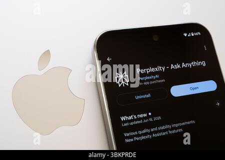 Perplexity download page displayed on smartphone beside silver Apple logo, illustrating app store availability across platforms. Stafford, United King Stock Photo