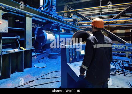 Factory engineer operates pipe painting automatic machine. Stock Photo