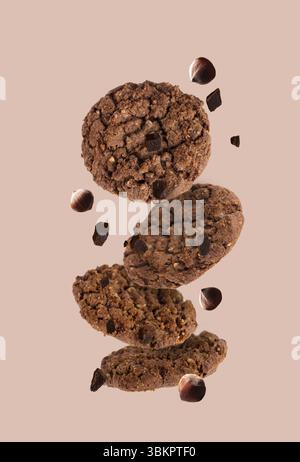 Chocolate chip cookies with crushed hazelnuts flying on a beige background Stock Photo