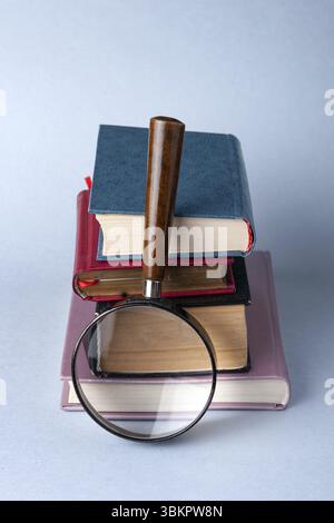 A stack of hardcover books and a magnifying glass on a blue background Stock Photo