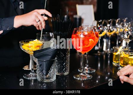 Close-up of a bartender mixing drinks at a stylish bar setup with vibrant cocktails, garnishes, and elegant glassware. Stock Photo