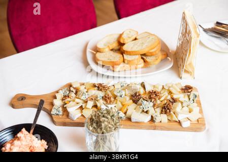 Elegant cheese platter featuring blue cheese, brie, hard cheeses, and walnuts, served with toasted bread slices on white tablecloth. Stock Photo