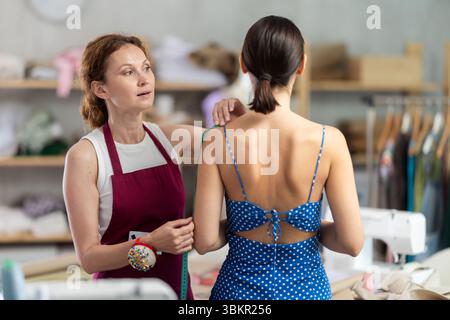 Woman tailor using measuring tape to measure clothes in sewing workshop Stock Photo