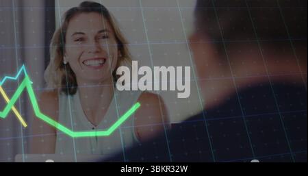 Smiling adult woman in white blouse reviewing data at office desk, with digital line graph overlay Stock Photo