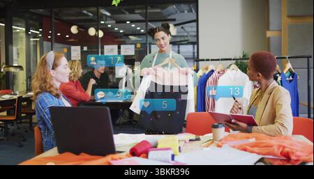 Presenting designer holding two-tone dress on hanger in open-plan workspace, with social icons Stock Photo