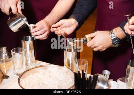 Close-up of bartenders mixing drinks using shakers, measuring spoons, and pouring ingredients during a cocktail-making session. Stock Photo