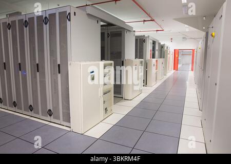 Server racks and PDUs lining 3D render data center corridor, showing tiles, fire piping and lights Stock Photo