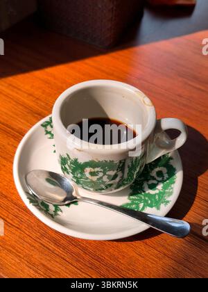 A cup of black coffee that has been drunk on a wooden table with morning light Stock Photo