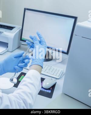 Lab technician in gloves analyzing samples with scientific glassware and computer in a modern medical laboratory Stock Photo