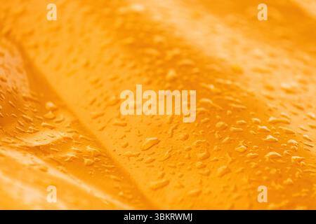 Raindrops on smooth yellow metallic industrial object surface, weather and climate concept, selective focus Stock Photo