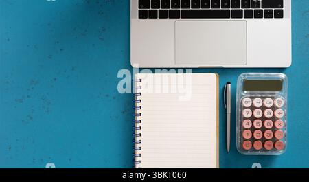 Office desk workspace with laptop, notebook, pen and calculator on blue background, directly above Stock Photo