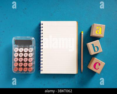 School supplies including calculator, blank notebook and abc wooden blocks on a blue background, concept of back to school or learning Stock Photo