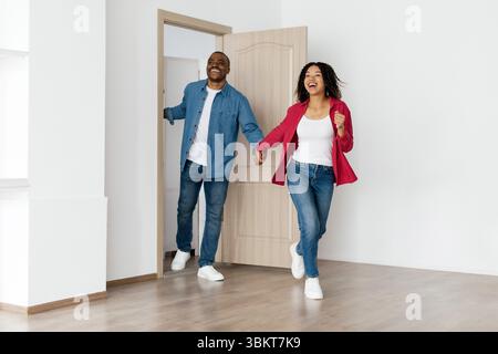 New House. Excited black couple rushing into apartment, holding hands and laughing Stock Photo