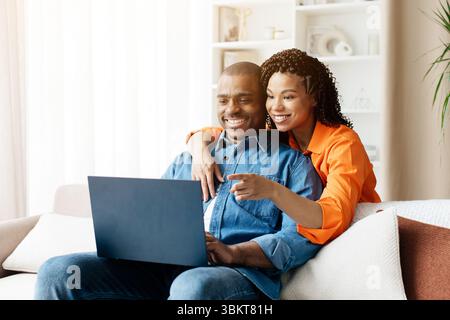 Black couple sitting on cozy sofa at home, using laptop together Stock Photo