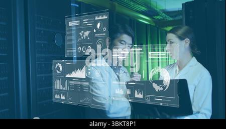 Two IT experts analyzing floating data holograms in server room corridor, with laptop and stylus Stock Photo