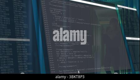 Office monitor displaying JavaScript code in dimly lit workstation, with glass partition reflection Stock Photo