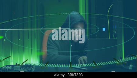 Monitoring hacker in hoodie scanning laptop and circuit board in data center, holographic overlay Stock Photo