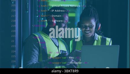 IT technicians in neon vests checking laptop code in server room, with headphones and server racks Stock Photo