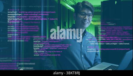 Standing Korean man holding laptop inside server room, with server racks and overlaid code text Stock Photo