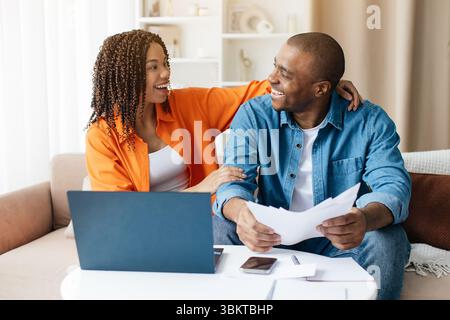 Happy African American couple smiling while reading financial papers at home Stock Photo