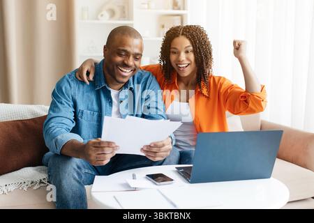 Excited young black spouses with papers celebrating good news at home Stock Photo