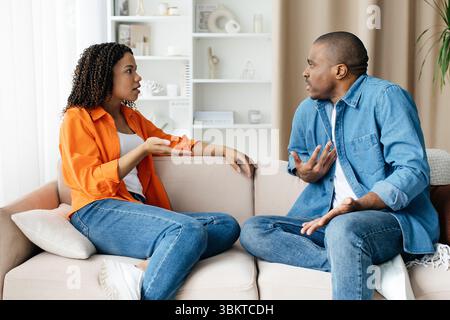 Black Couple Having Emotional Conversation While Sitting On Couch At Home Stock Photo