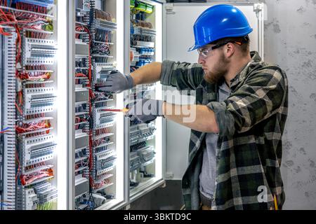Electrician inspects connection. Working inside switchboard. Tool in hand. Stock Photo