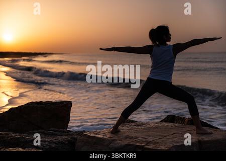 Woman Practicing Yoga at Sunrise on Beach. Stock Photo