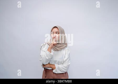 Keep silence. young indonesian woman wearing hijab keeps finger on lips showing sign of silence. isolated white background Stock Photo