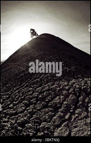 A young man rides his dirt bike up and over a steep hill while motocross riding the surreal dunes near Cameron, AZ. Stock Photo