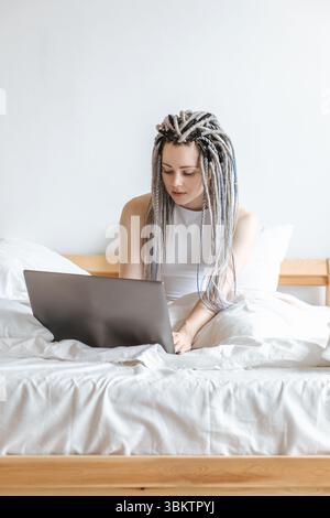 Woman working on computer, laptop in white bed. Stock Photo