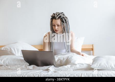 Young woman working on computer, laptop in white bed. Stock Photo